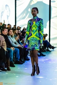 A model wearing a bright green and blue mini dress walks the runway