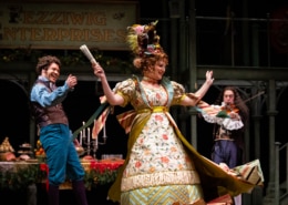 A man claps while a woman dances, her skirts flying. A man with a violin plays in the background.