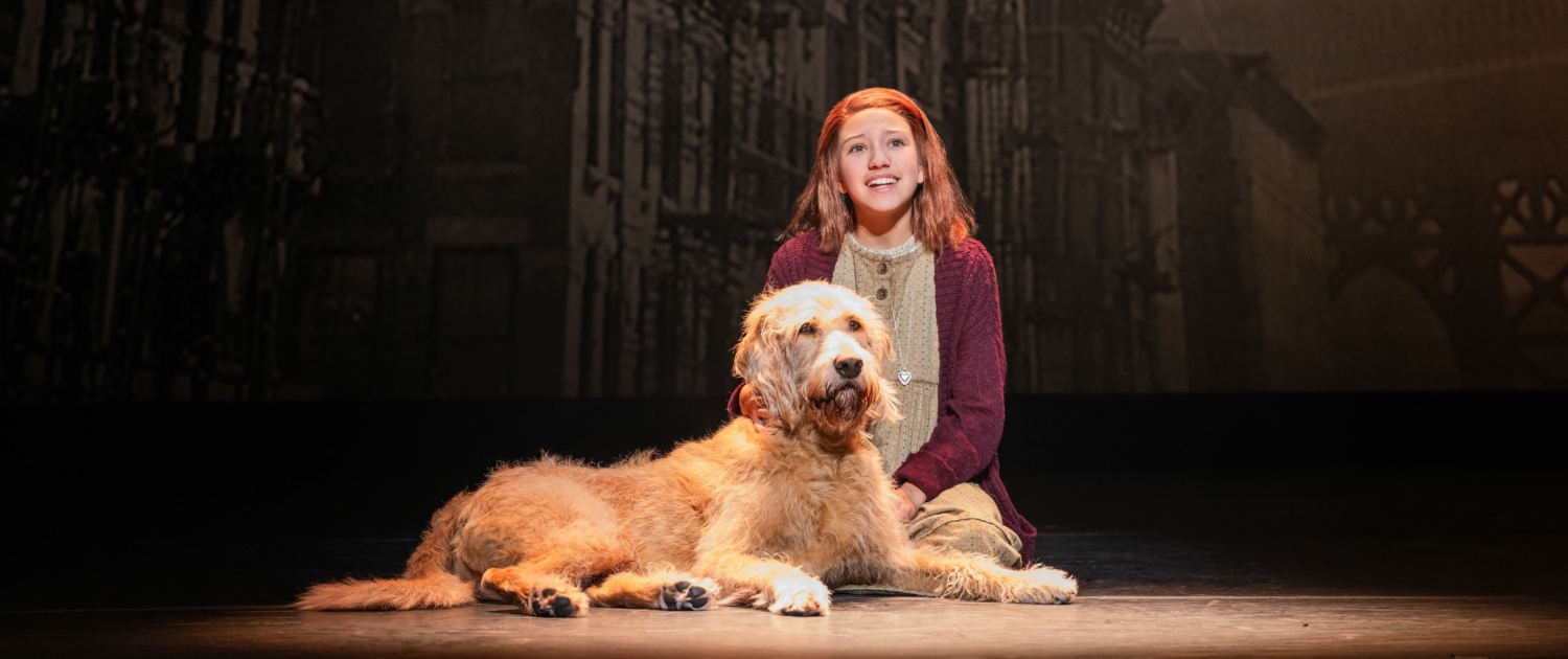 A young girl sits on the ground with her shaggy dog.