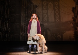 A young girl in raggedy clothes stands with a sandy-colored shaggy dog.