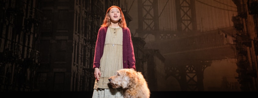 A young girl in raggedy clothes stands with a sandy-colored shaggy dog.