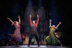 Two women (left and right) and a man (center) dance with their arms extended in the air. They are all wearing forties era clothing.
