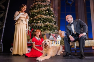 A woman dressed in an elegant gown and a man dressed in a tuxedo look down at a young girl and her dog.