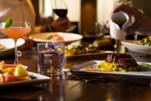 A table filled with dinner delights, like steak and roasted potatoes, and cocktails.