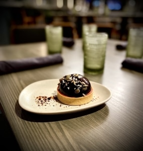An elegant, petite tart with a rounded top sits on a plate.