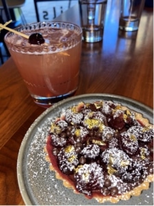 A berry tart dusted with powdered sugar next to a pink cocktail