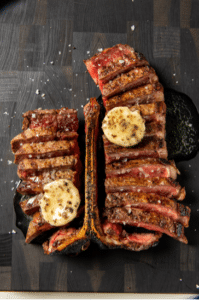 A large steak sliced and removed from the bone, pats of butter on top.