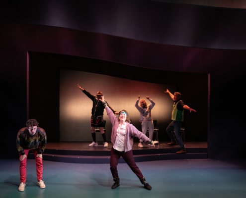A young man in a colorful sweater leans over clasping his knees. His grandparents are wearing headbands and doing a Jazzercise routine next to him.