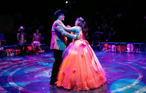 A teenage girl in a pink quinceañera dress dances with her father who is wearing a tan blazer and a black cowboy hat.