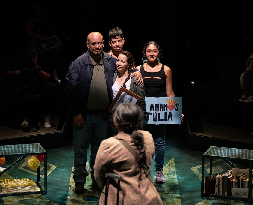 A teenage girl in a brown plaid blazer looks at her family as they bid her farewell.