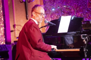 A man sits at a piano, wearing a red suit.