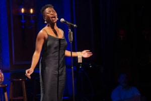 A woman sings into a microphone on a stand. She is wearing a black silk dress