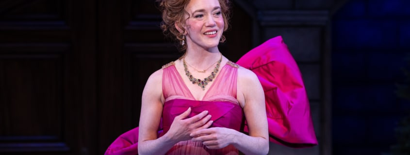 Emma smiles to someone on her left, outside the frame. She's wearing a hot pink gown with a large bow at the back.