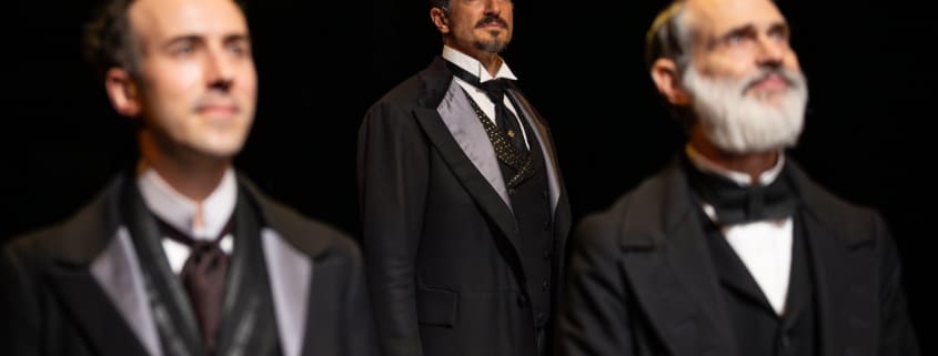 Two men stand in the foreground, another slightly behind. They're looking off into the distance. All are wearing old fashioned three piece suits.
