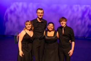 Camille, Caleb, Gabi, and Connor pose for a photo together, smiling. They are all in black formal wear.