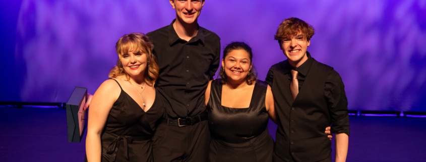 Camille, Caleb, Gabi, and Connor pose for a photo together, smiling. They are all in black formal wear.