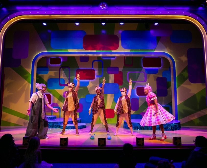 Gerald the Elephant and Piggie look at each other across the stage, the three Squirrelles dance in unison with one hand pointed up in the air