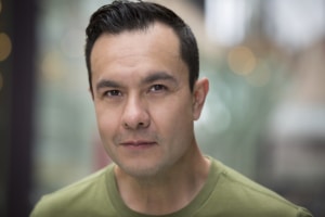 Denver actor Rodney Lizcano wearing a green shirt, standing outdoors with a soft-focus background.